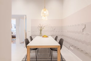 A dining area with a white table, black chairs, a patterned rug, and a hanging light fixture. - Venus Apartments - Opera (Budapest)