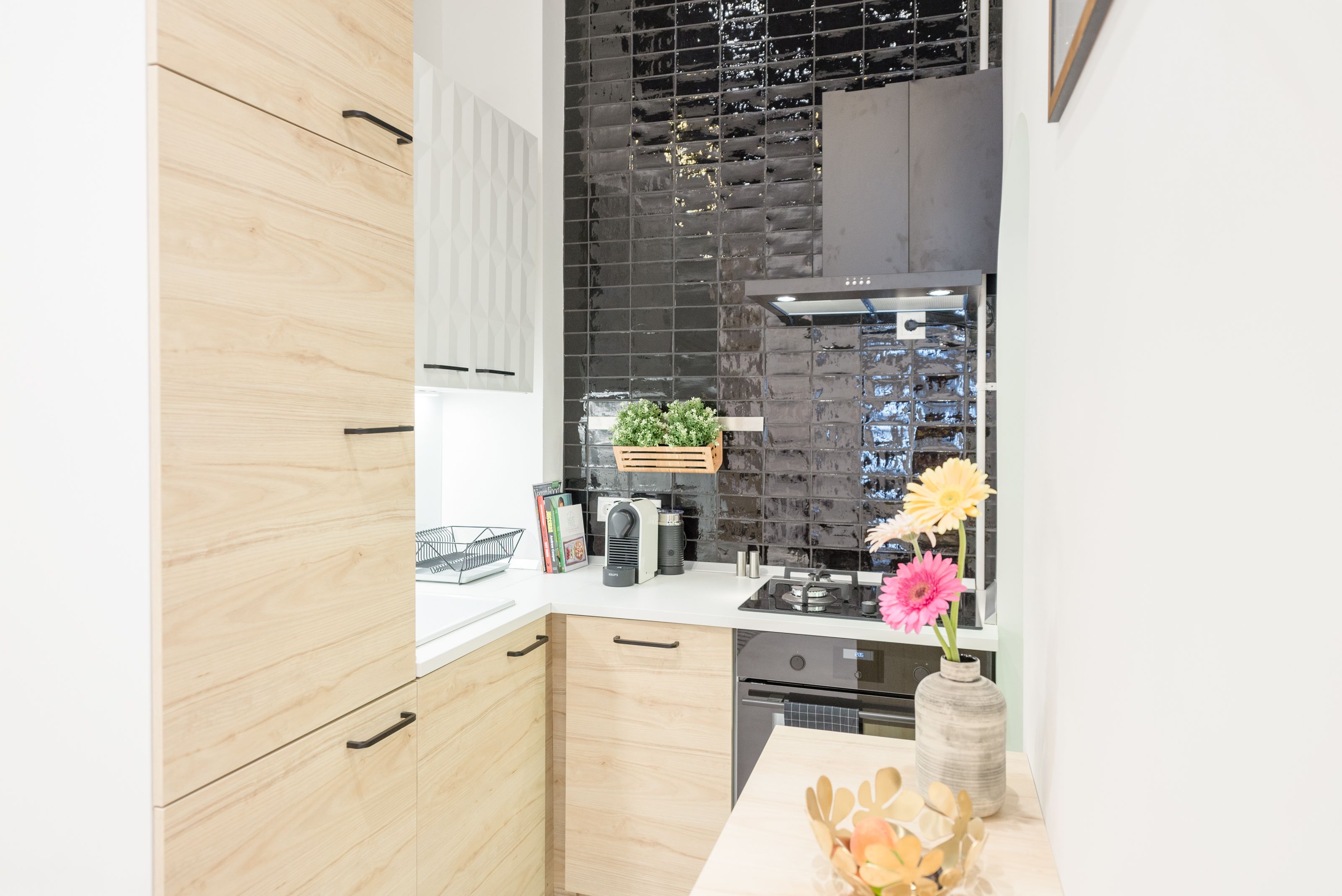 A modern kitchen with wooden cabinets, a black backsplash, and a vase with flowers on the counter.