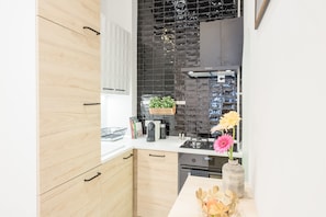 A modern kitchen with wooden cabinets, a black backsplash, and a vase with flowers on the counter. - Venus Apartments - Opera (Budapest)
