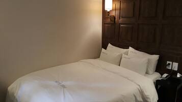 Una cama bien hecha con ropa de cama blanca y almohadas que dicen "HOTEL 20BY", en una habitación con paneles de madera en la pared y una mesita de noche con una lámpara y un teléfono.