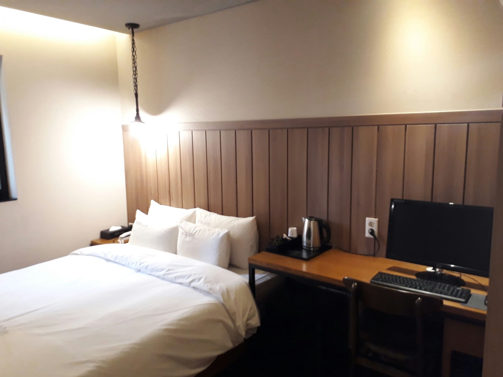 A hotel room with a bed, a desk with a computer, a chair, and a coffee maker.