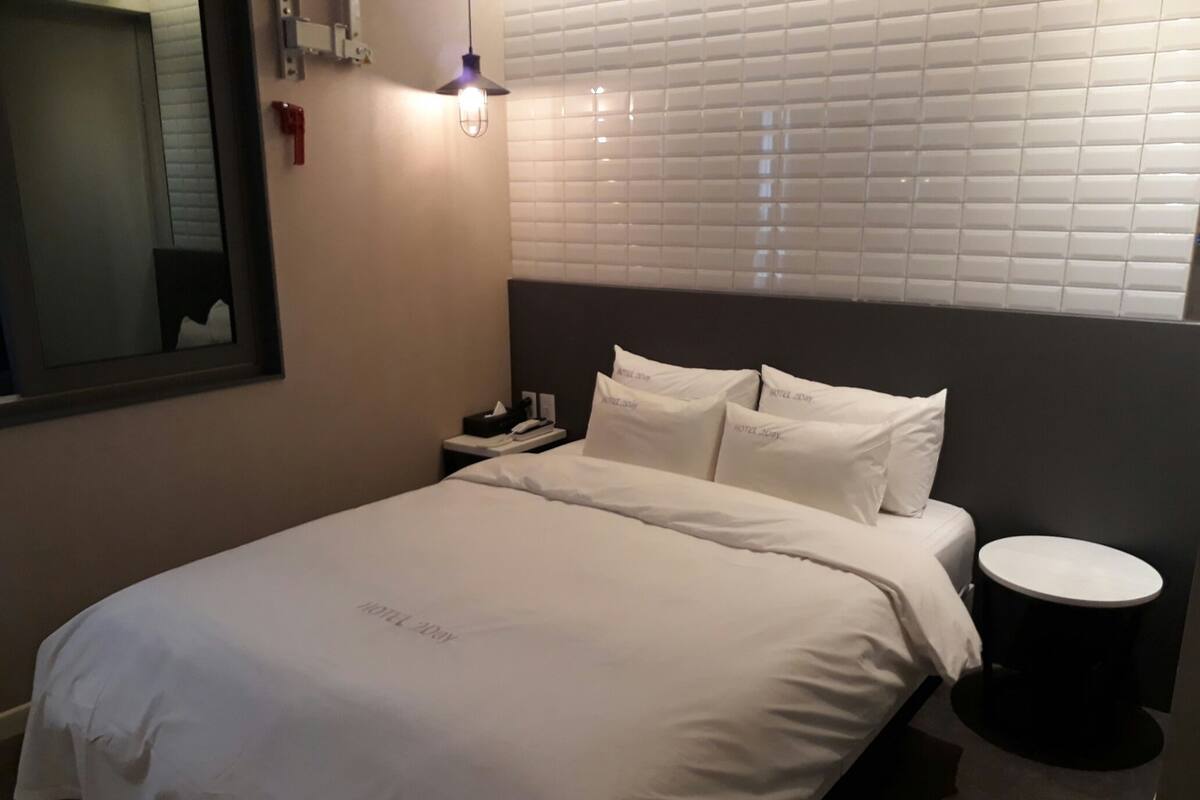 A neatly made bed with white linens, a bedside table with a lamp, and a wall-mounted light fixture.