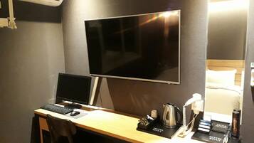 Habitación de hotel con escritorio, dos monitores, cafetera, teléfono y cama con cabecera.