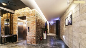 A hallway with a brick wall, an elevator, and a tiled floor. - 2day Hotel (Geoje)
