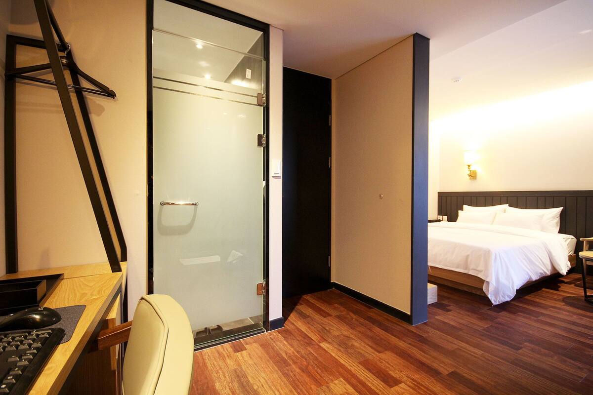 A hotel room with a desk, chair, bed, and a glass door leading to a shower area.