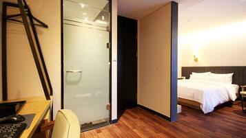 A hotel room with a desk, chair, bed, and a glass door leading to a shower area.