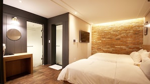 A bedroom with a large bed, a wooden desk, a mirror, and a brick wall. - 2day Hotel (Geoje)