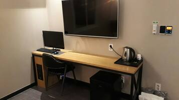 Habitación de hotel con escritorio, televisor, teclado, silla, cesto de basura, tetera y minibar.