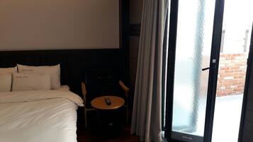 Une chambre d’hôtel avec un lit, une petite table sur laquelle se trouve une télécommande, et une vue sur l’extérieur à travers une porte vitrée.