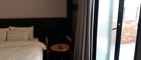 Habitación de hotel con una cama, una mesita con un control remoto y vistas a través de un ventanal.