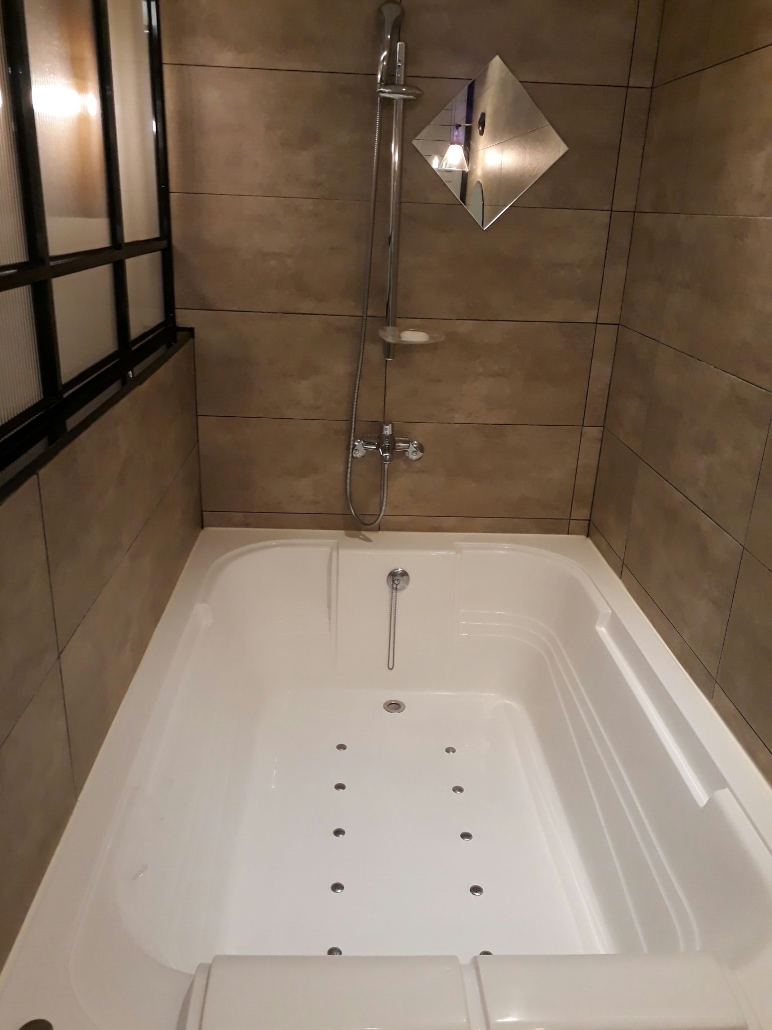 A bathroom with a white bathtub, a showerhead, and a mirror on the wall.