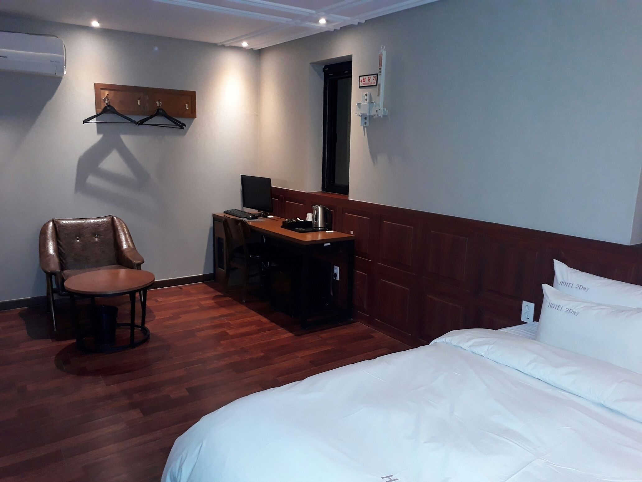 A hotel room with a bed, a desk with a computer, a chair, and a coat rack.