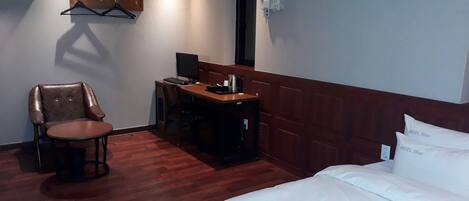 A hotel room with a bed, a desk with a computer, a chair, and a coat rack.