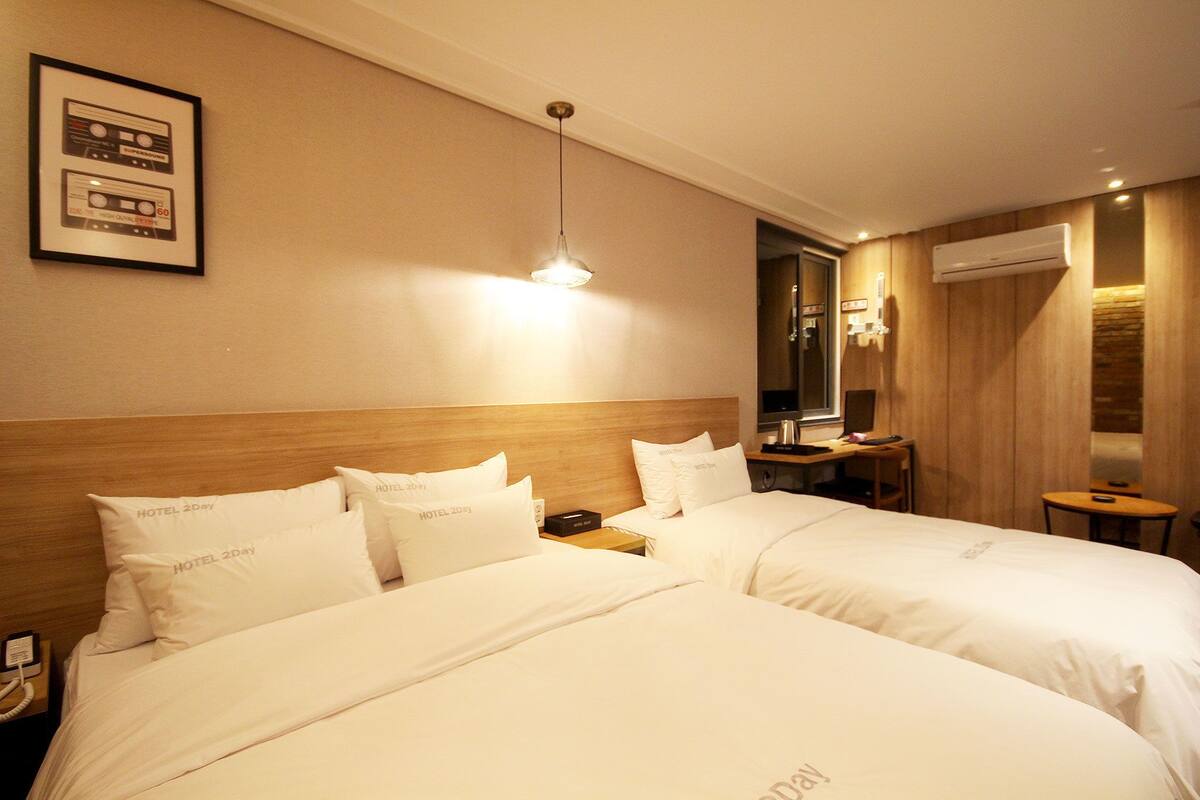A hotel room with two beds, a nightstand, a desk, and a mirror.