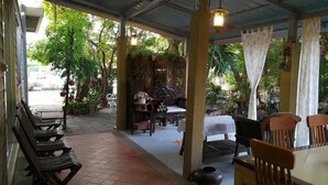 A covered outdoor seating area with wooden benches and tables, surrounded by potted plants and trees. - Nonnaisuan resort (Bangkok)