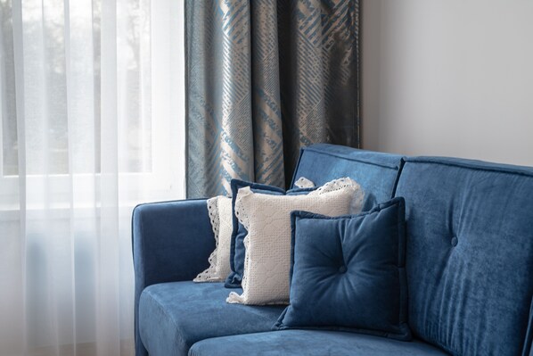 A blue sofa with white and blue cushions in a room with sheer curtains and patterned drapes.