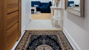 Un couloir avec une porte en bois, une console blanche surmontée d’un vase de fleurs, un canapé bleu et un grand miroir.