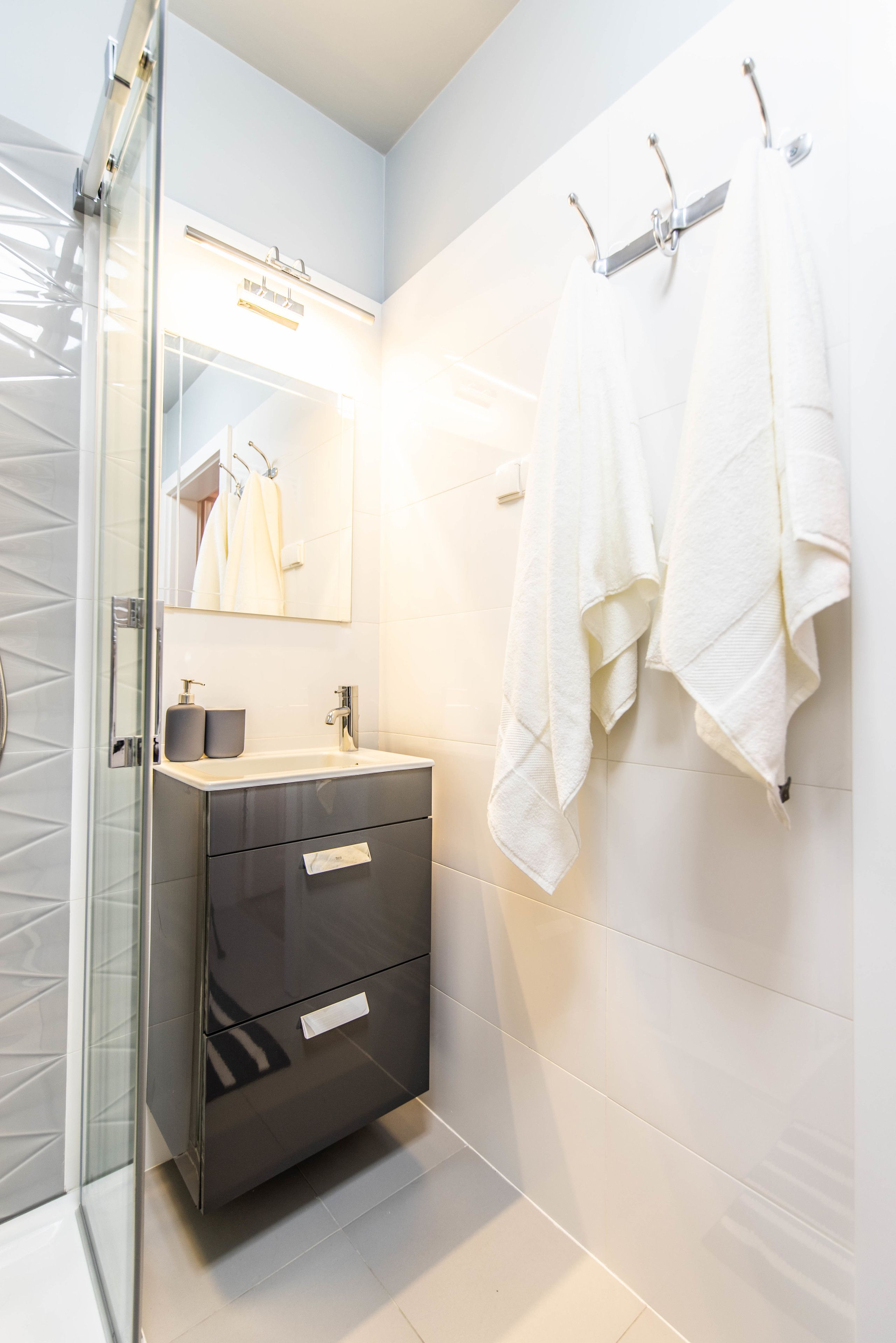 Une salle de bain moderne avec une douche à parois de verre, un meuble-lavabo foncé doté d’un miroir et des serviettes blanches suspendues à un porte-serviettes.