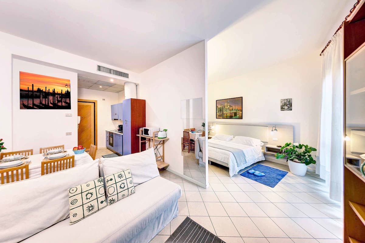A modern hotel room with a bed, a sofa, a dining area, and a kitchen.