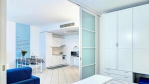 Une cuisine moderne avec des meubles blancs, un four à micro-ondes et un coin repas comprenant une chaise et une table bleues.