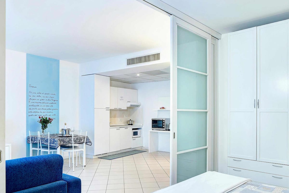 A modern kitchen with white cabinets, a microwave, and a dining area with a blue chair and table.
