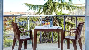 Un balcon avec une table dressée pour deux personnes, agrémentée d’un vase de fleurs, d’un saladier de fruits et de verres.