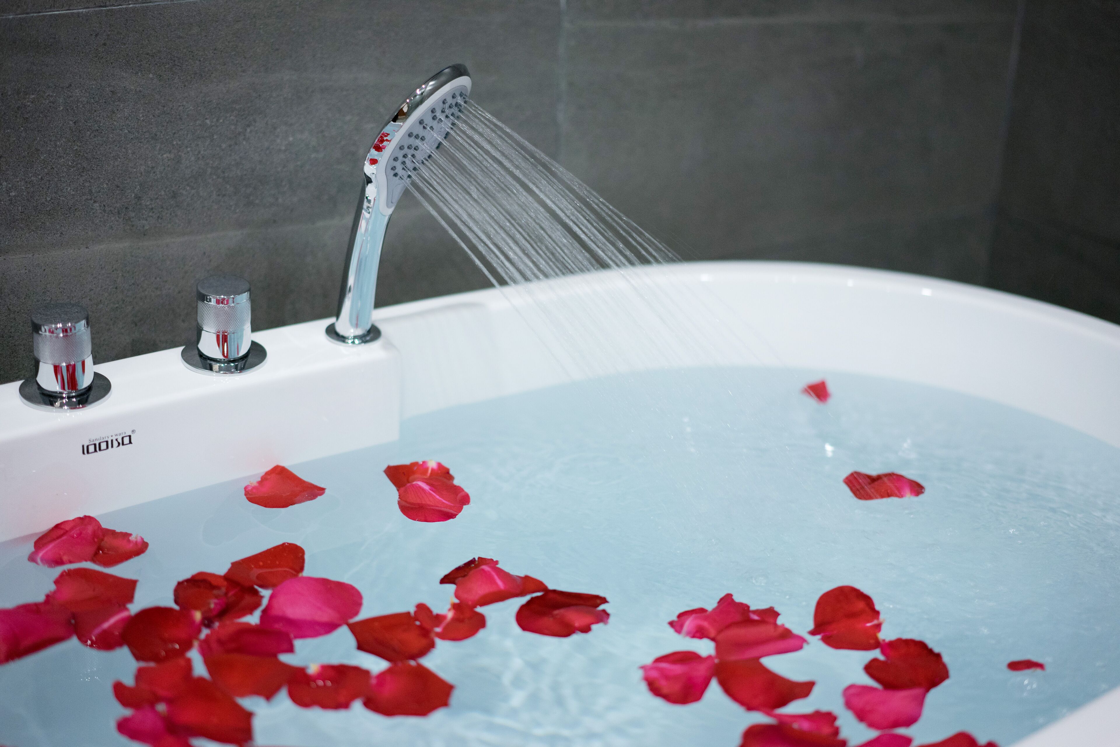 A bathtub with rose petals floating in the water and a showerhead above it.