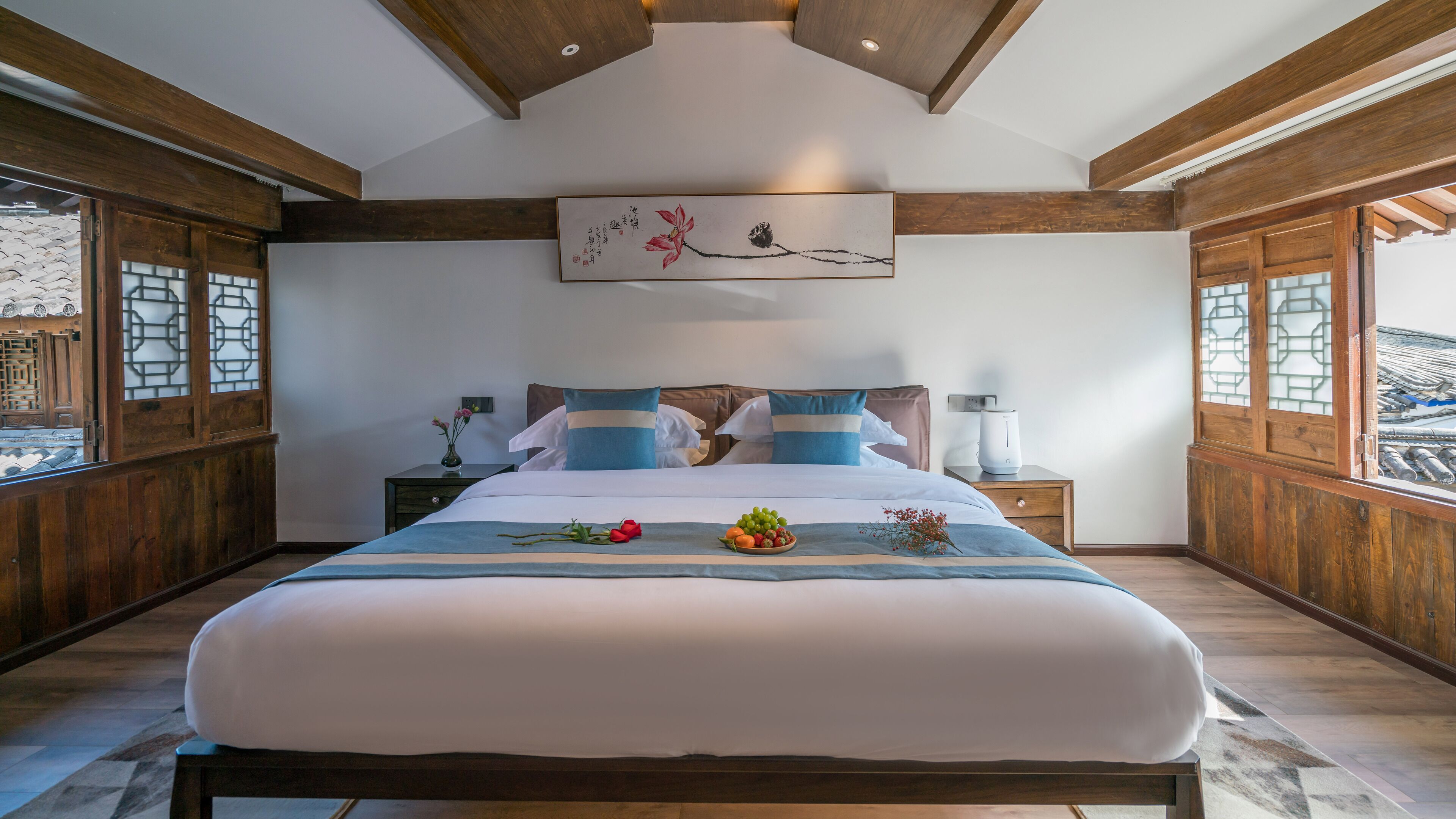 A bedroom with a large bed, wooden beams, a painting, and a nightstand with a lamp.