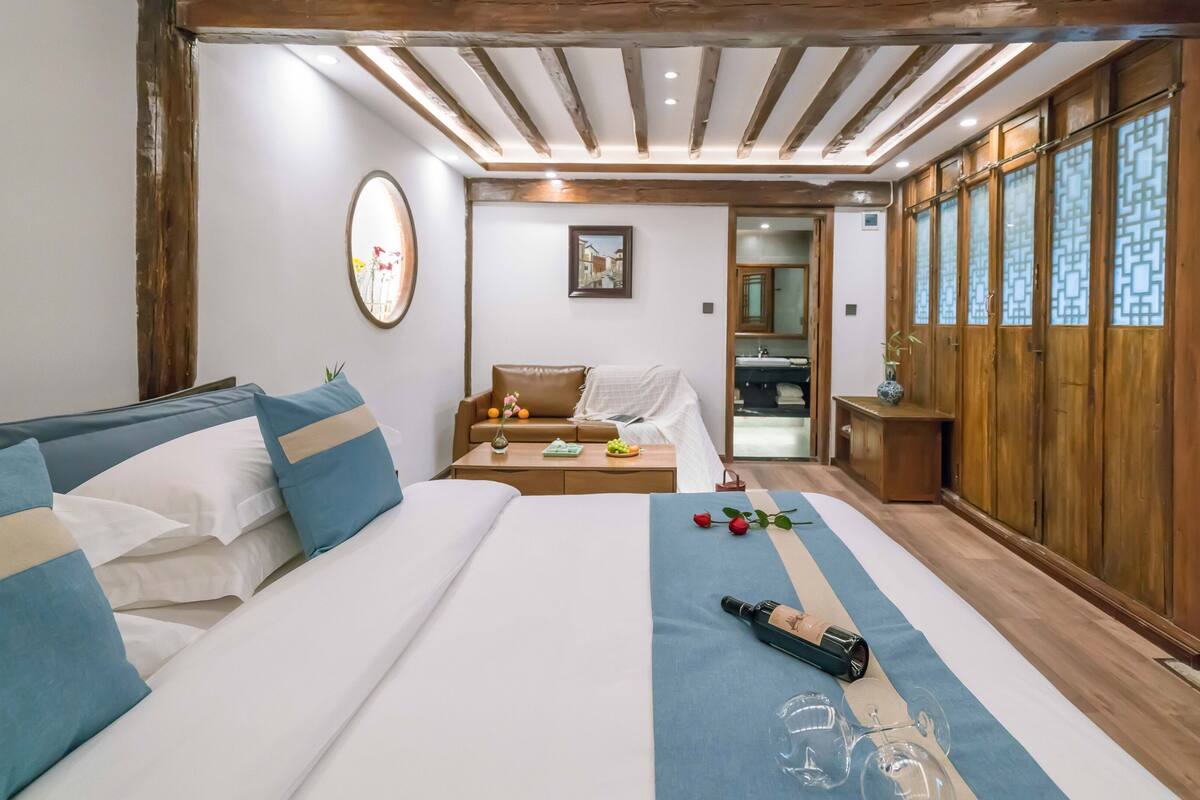 A bedroom with a large bed, a nightstand, a dresser, and wooden wardrobe doors.