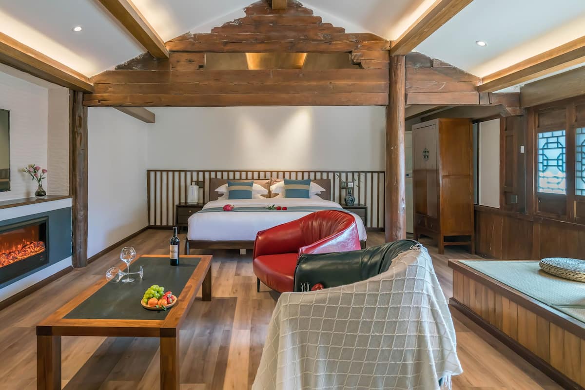 A modern hotel room with a large bed, a fireplace, a TV, and a dining area with fruit.