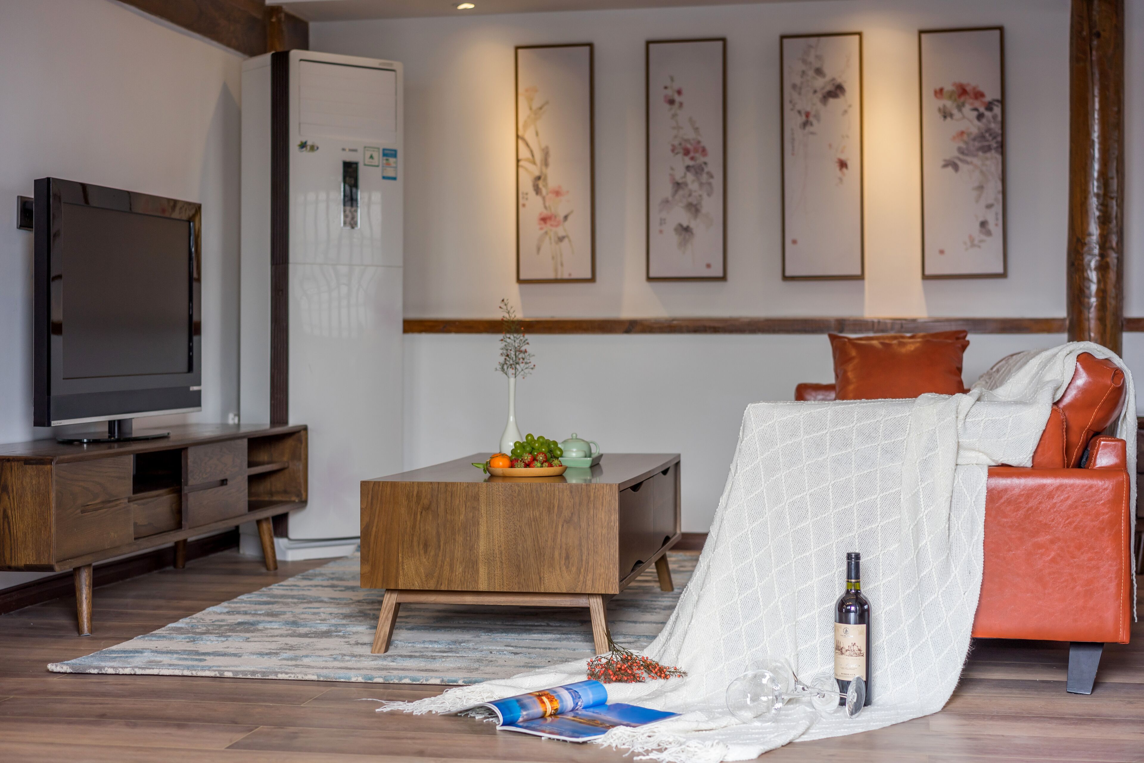 Una sala de estar con televisor, muebles de madera, una mesa de centro con frutas y un sofá con una manta.