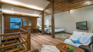 A room with a wooden ceiling, a bed with a blue and white bedspread, a television mounted on the wall, and a wooden table with a fruit bowl. - Lize Graceland Artistic Suite Inn (Lijiang)