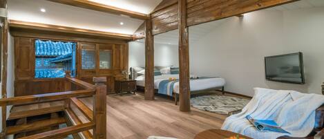 A room with a wooden ceiling, a bed with a blue and white bedspread, a television mounted on the wall, and a wooden table with a fruit bowl.