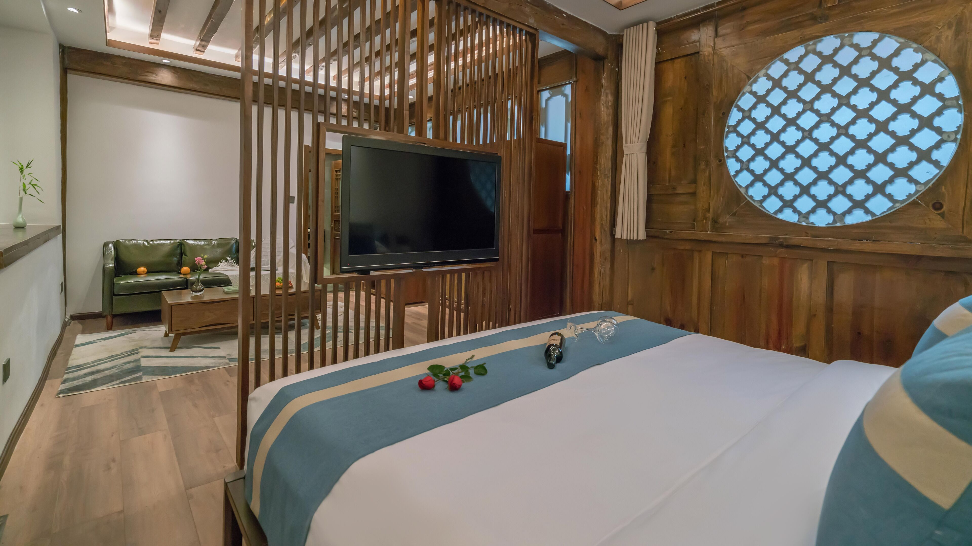 Een slaapkamer met een houten plafond, een televisie, een bed met een blauw-witte dekbedovertrek en een houten scheidingswand.