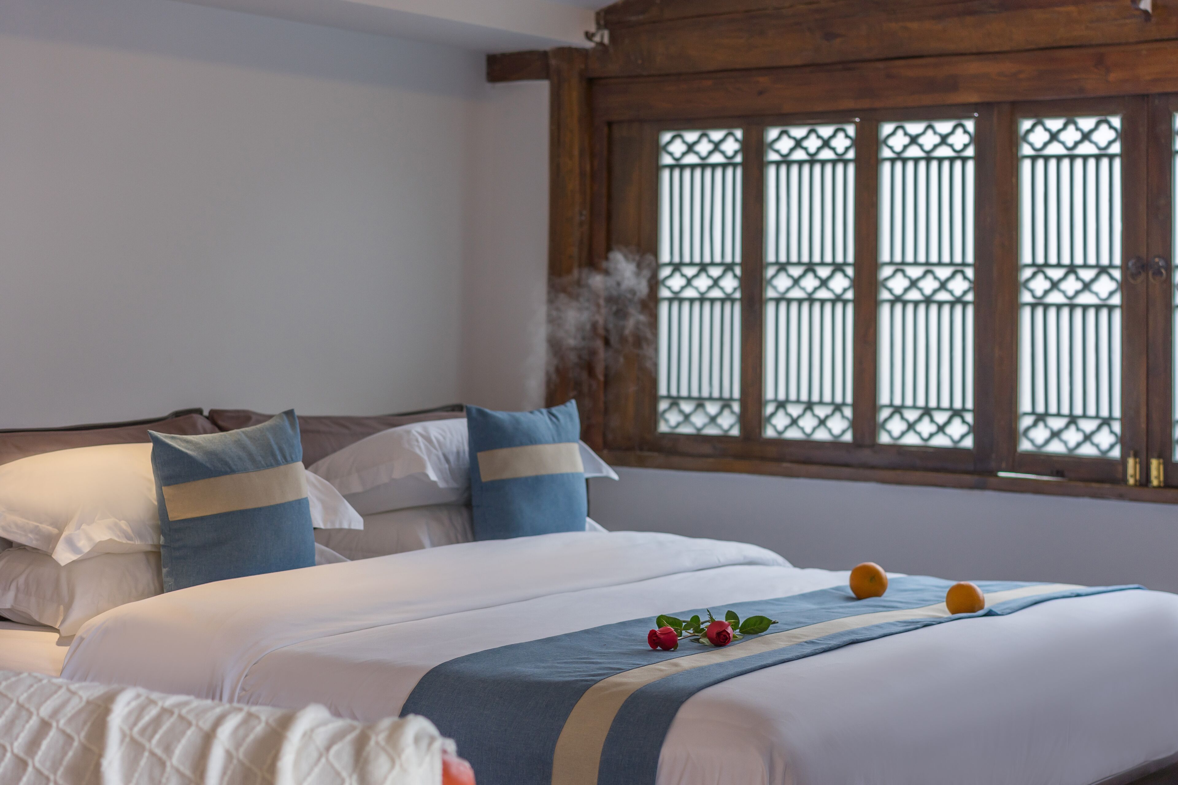 A hotel room with a large bed, a window with wooden frames, and a decorative plant.