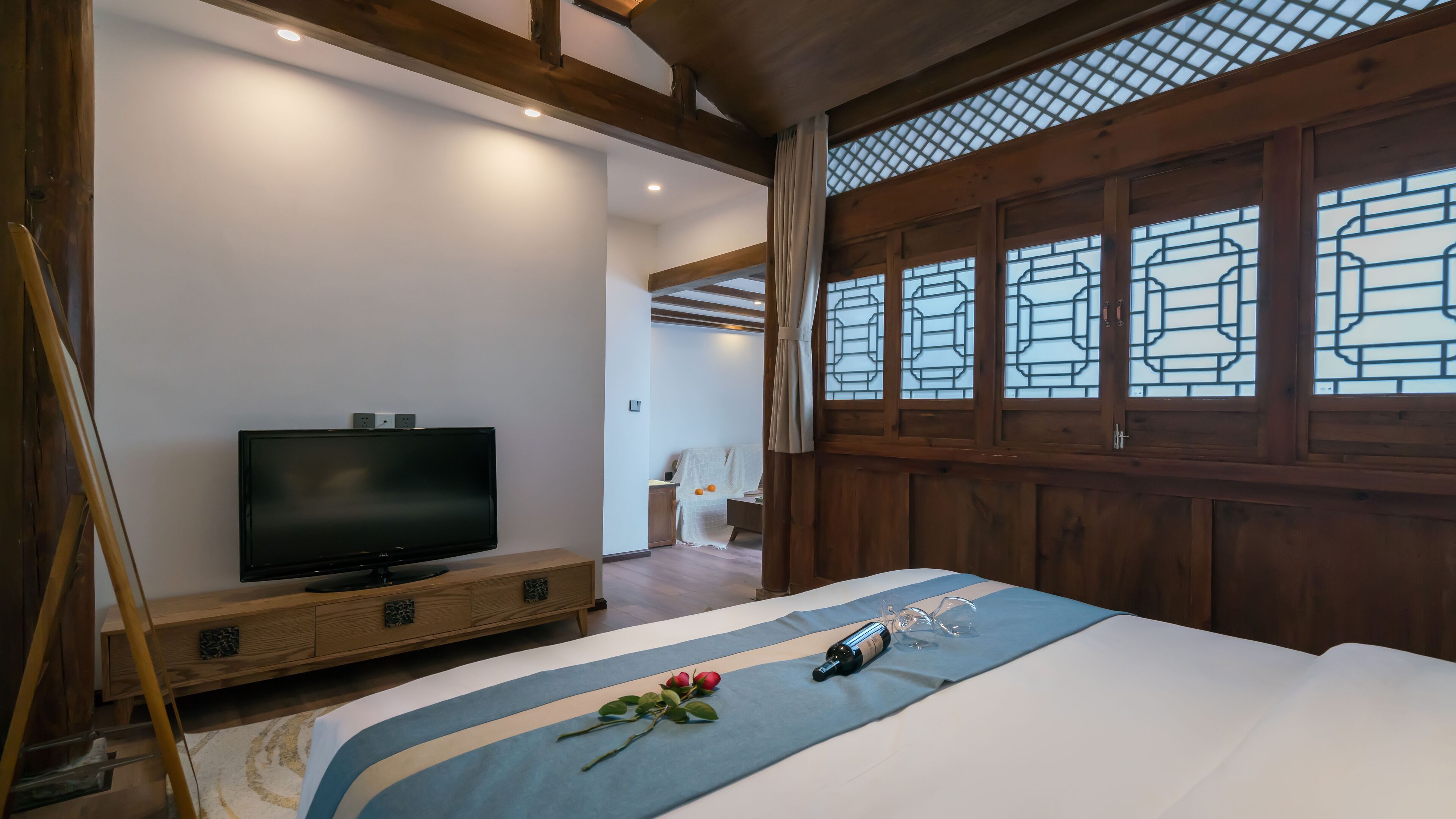 A bedroom with a TV on a wooden stand, a bed with a blue and white bedspread, and a wooden wardrobe.