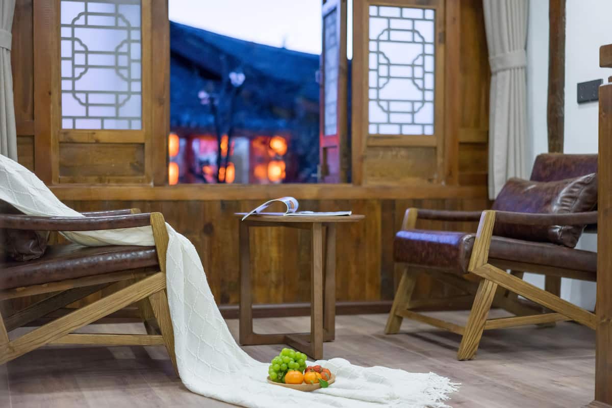 A traditional room with wooden furniture, a small table with a fruit bowl, and a view of a traditional building through a window.