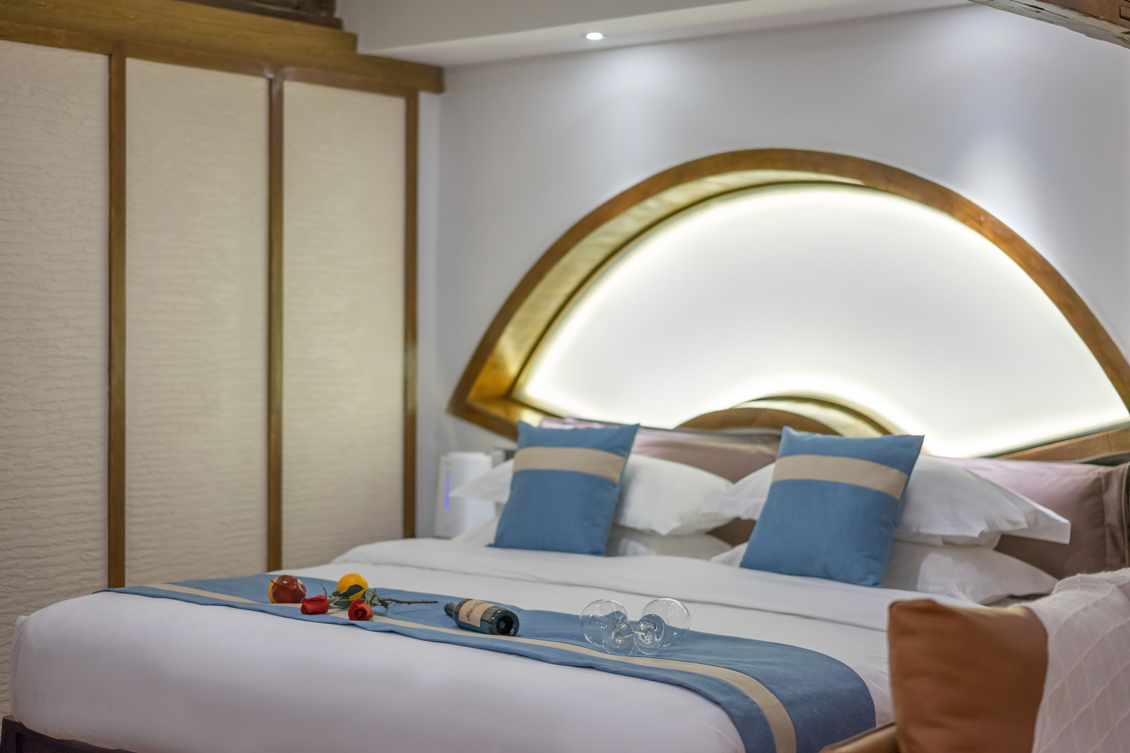 Een hotelkamer met een net opgemaakt bed, een nachtkastje met een fles en glazen, en een hoofdbord met een lamp.