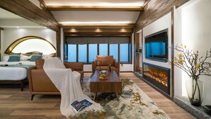 A modern hotel room with a bed, a sofa, a coffee table with fruit, a fireplace, and a TV. - Lize Graceland Artistic Suite Inn (Lijiang)