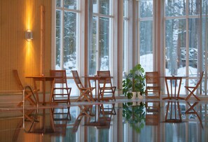 A room with large windows, wooden chairs, a glass table, and a potted plant. - Sätra Brunn Hälsobrunn (Sala)