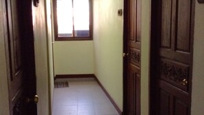 A narrow hallway with a tiled floor, a window with blinds, and a door with a decorative panel. - BC guesthouse Banglamphu (Bangkok)