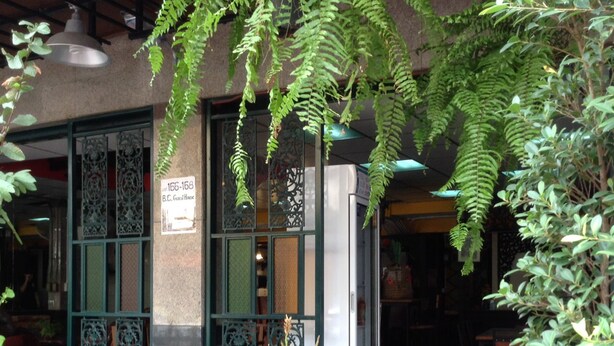 An outdoor seating area with a wooden bench and potted plants, a building entrance with decorative metalwork, and a sign indicating a guest house. - BC guesthouse Banglamphu (Bangkok)