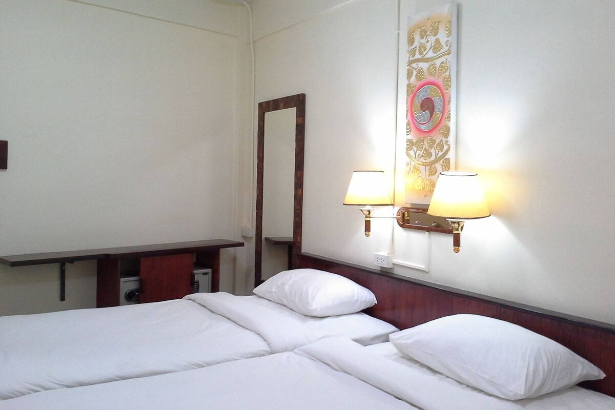 A hotel room with two single beds, a bedside table, a mirror, and two wall-mounted lamps.