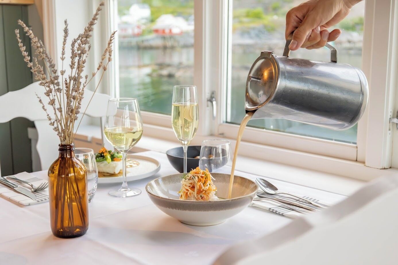A dining table with a bowl of pasta, two wine glasses, and a bottle of wine.