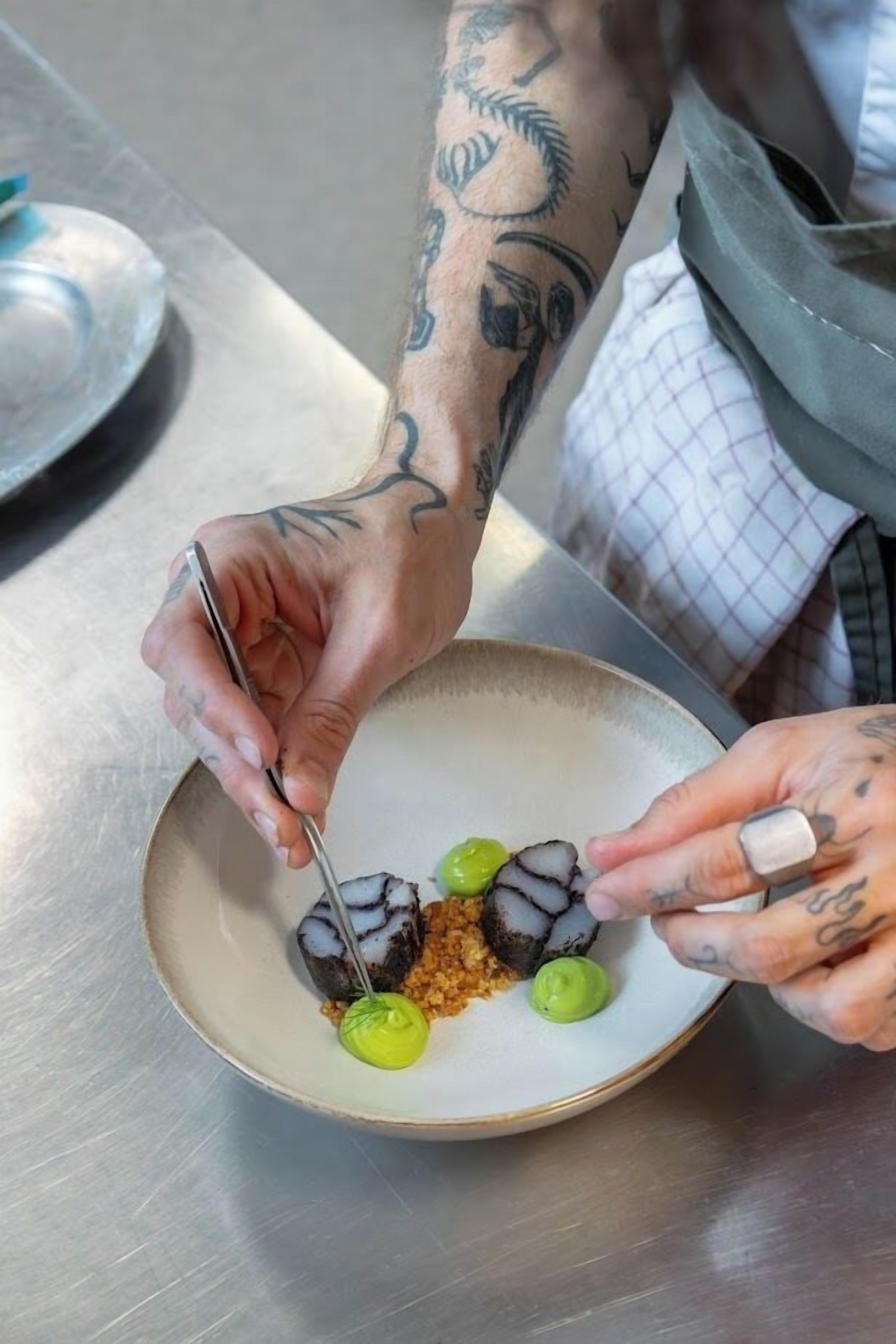 A person with tattoos preparing food on a plate.