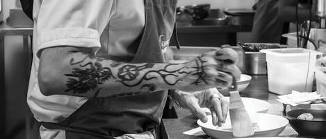 Uno chef prepara dei cibi in una cucina con piani di lavoro in acciaio inossidabile e diversi utensili da cucina.
