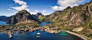 Un pueblo costero con casas y barcos, rodeado de acantilados escarpados y un cielo azul cristalino.