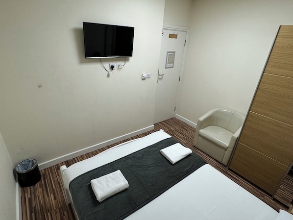 Una habitación de hotel con cama, televisión montada en la pared, una silla y un armario.