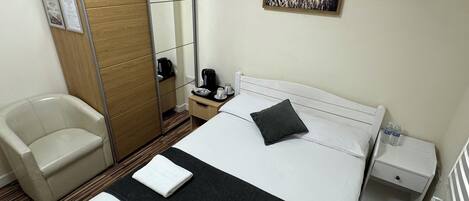 Una habitación de hotel con una cama, una silla, una mesita de noche, un espejo y un cuadro en la pared.