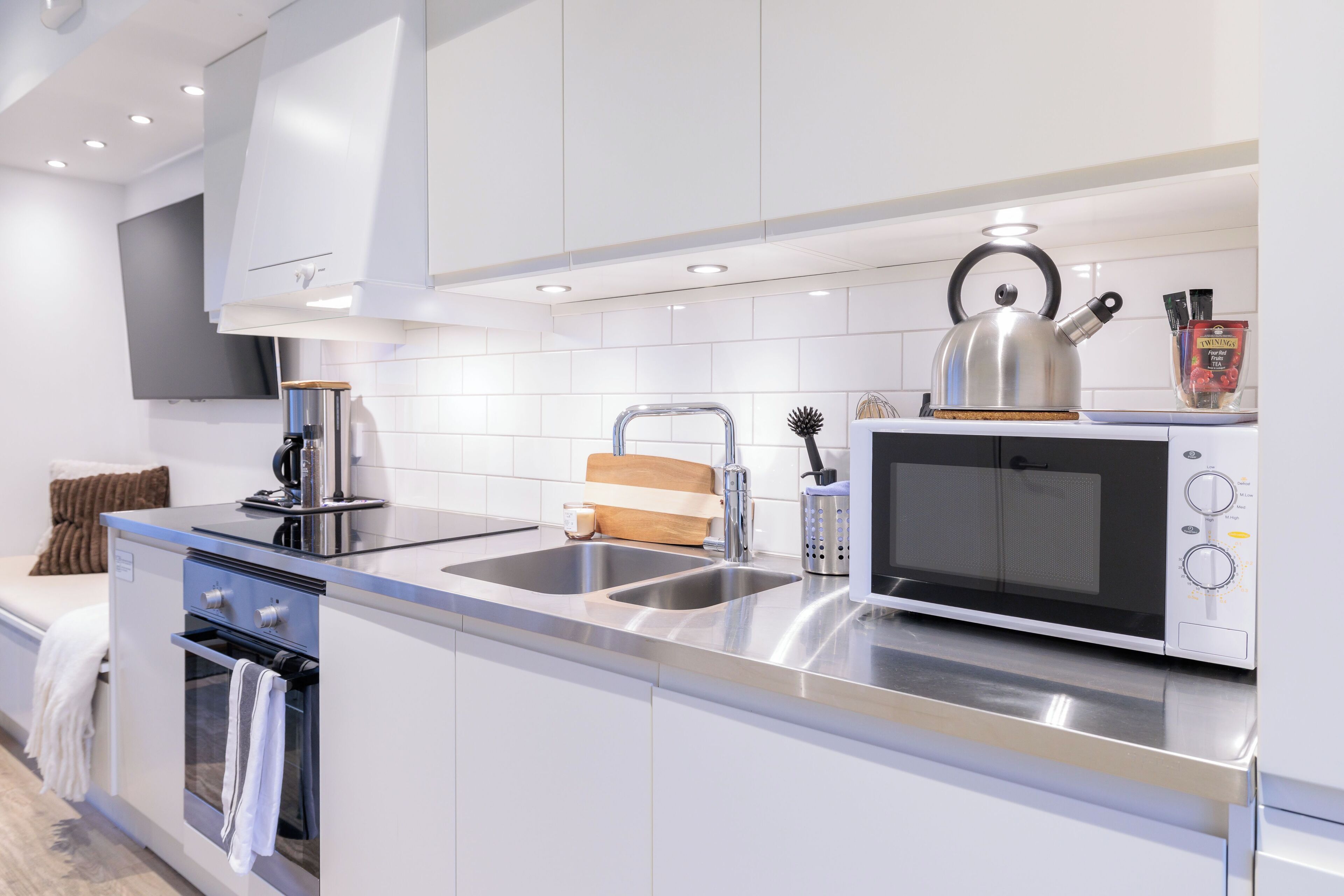 Una cocina moderna con electrodomésticos de acero inoxidable, horno empotrado, microondas y hervidor sobre la encimera.